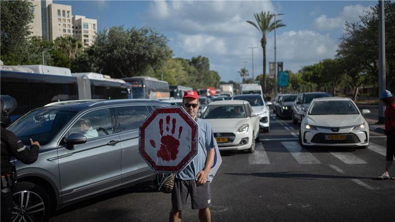 Streik in Israel aus Solidarität mit den Hamas-Geiseln Ein israelischer Demonstrant geht mit einem Schild auf einer Straße, während Autos sich stauen.