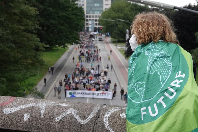 Fridays for Future: Klima und Frieden sind untrennbar verbunden Ein junger Mann mit einer Fahne mit dem Logo von Fridays for Future verfolgt von einer Brücke aus die Demonstration des Bündnisses Fridays for Future. Das Bündnis Fridays for Future demonstriert bundesweit für mehr Klimaschutz und Konsequenzen nach der Hochwasserkatastrophe. Foto: Luise Evers/dpa