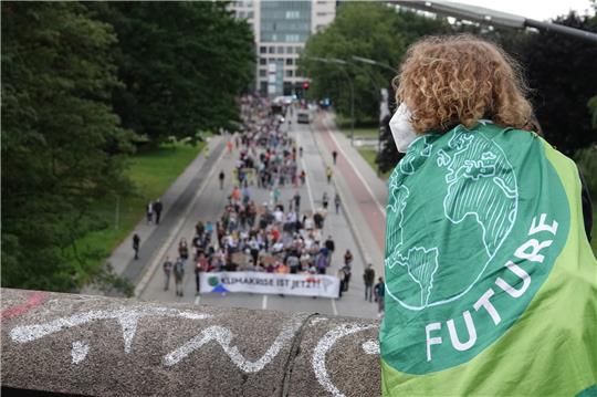 Ein junger Mann mit einer Fahne mit dem Logo von Fridays for Future verfolgt von einer Brücke aus die Demonstration des Bündnisses Fridays for Future. Das Bündnis Fridays for Future demonstriert bundesweit für mehr Klimaschutz und Konsequenzen nach der Hochwasserkatastrophe. Foto: Luise Evers/dpa