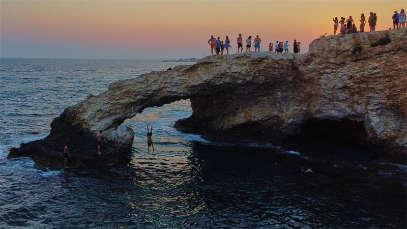 Ein junger Mann springt bei Sonnenuntergang im Ferienort Ayia Napa auf der im östlichen Mittelmeer gelegenen Insel Zypern von der natürlichen „Liebesbrücke“ ins Meer.