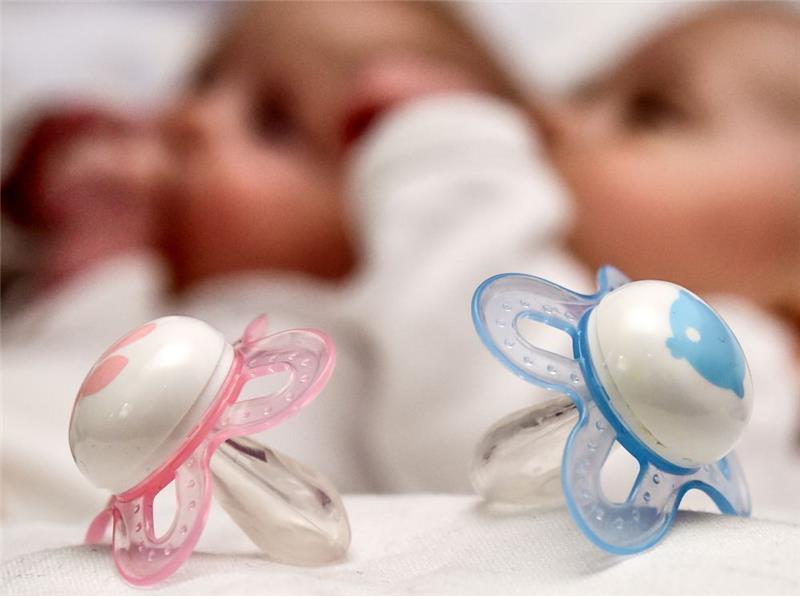 Ein rosa und ein blauer Schnuller vor zwei Babys. Archivfoto: Patrick Pleul/dpa