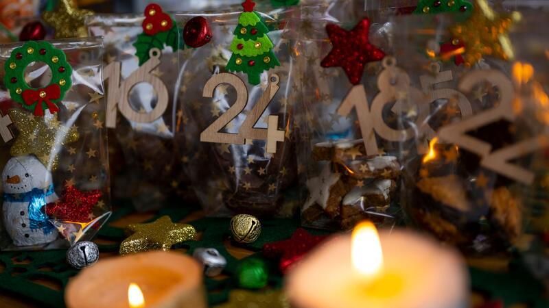 Ein selbstgemachter Adventskalender mit kleinen Tüten steht neben zwei Kerzen auf einem Tisch.