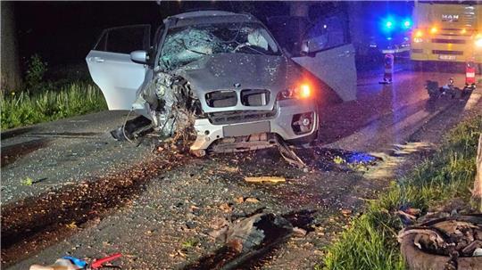 Ein stark beschädigter BMW steht mitten auf der Fahrbahn, nachdem er mit einem Baum kollidiert ist.