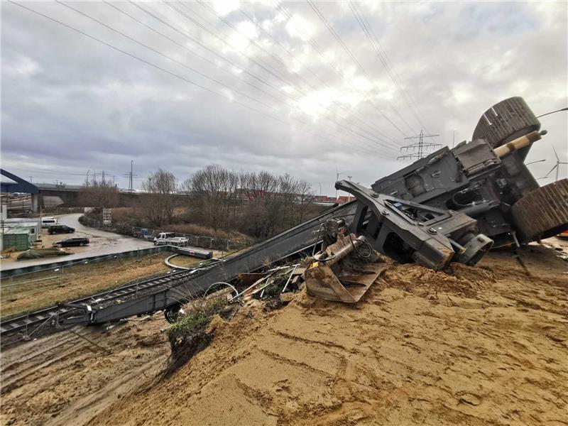 Ein umgekippter Bagger liegt an einer Böschung. Im Sturz riss der Bagger mit seinem Ausleger noch eine Stromleitung herunter. Foto: Steven Hutchings/TNN/dpa