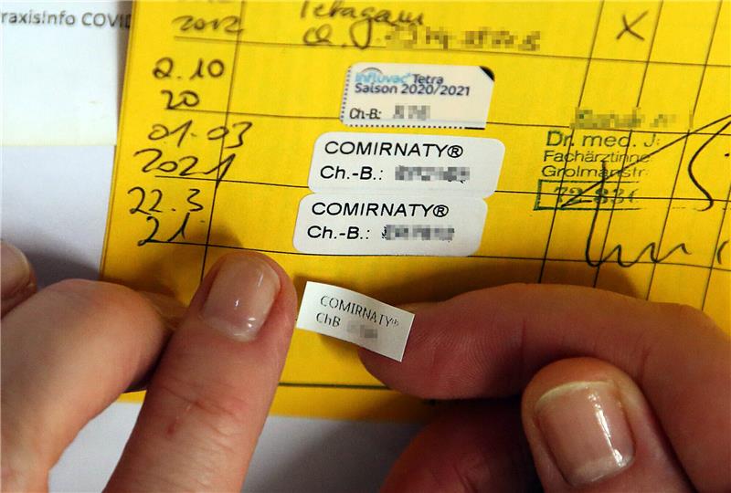 Eine Ärztin klebt den Nachweis für die dritte Impfung (Booster) mit dem Comirnaty-Impfstoff des Herstellers Biontech/Pfizer in ein Impfbuch. Foto: Wolfgang Kumm/dpa