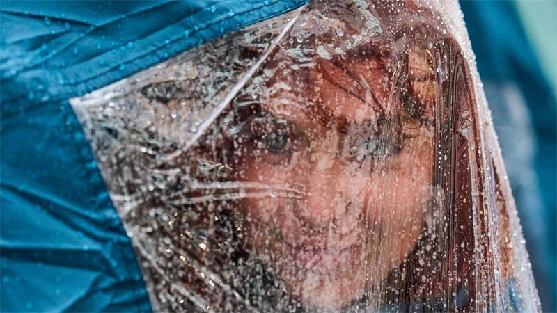 Eine Aktivistin blickt unter ihrer Regenkappe hervor, während sie bei starkem Regen auf dem Platz Puerta del Sol in Madrid an einem Protestcamp für das Recht auf Wohnen teilnimmt.