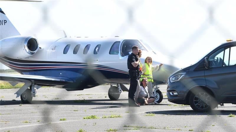 Farbattacke auf Privatjet auf Sylt: Haft für Klimaaktivistinnen Eine Aktivistin der Letzten Generation sitzt neben einem kleinen Flugzeug auf dem Flughafen auf Sylt.