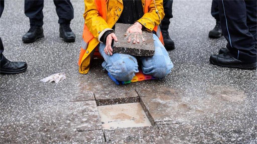 Eine Aktivistin sitzt mit einem Betonteil an ihrer Hand zwischen Polizisten auf ...