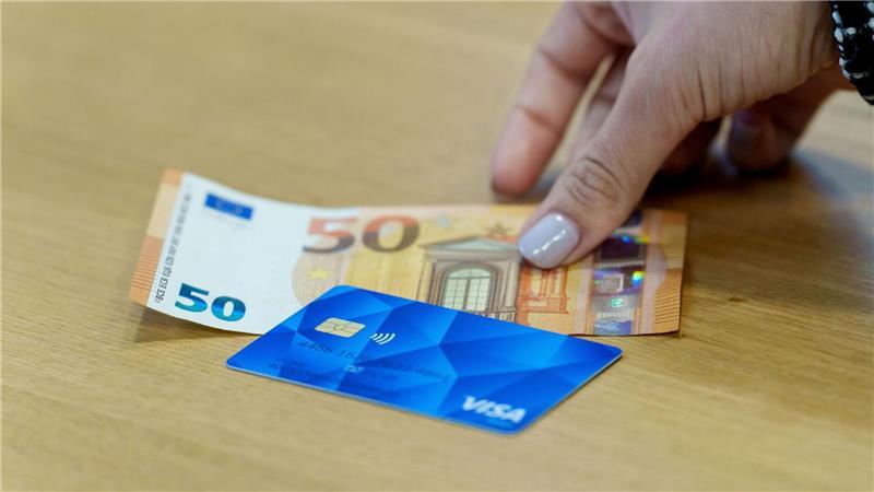 Eine Bezahlkarte für Asylbewerberinnen und Asylbewerber und ein 50-Euro-Schein liegen nebeneinander.