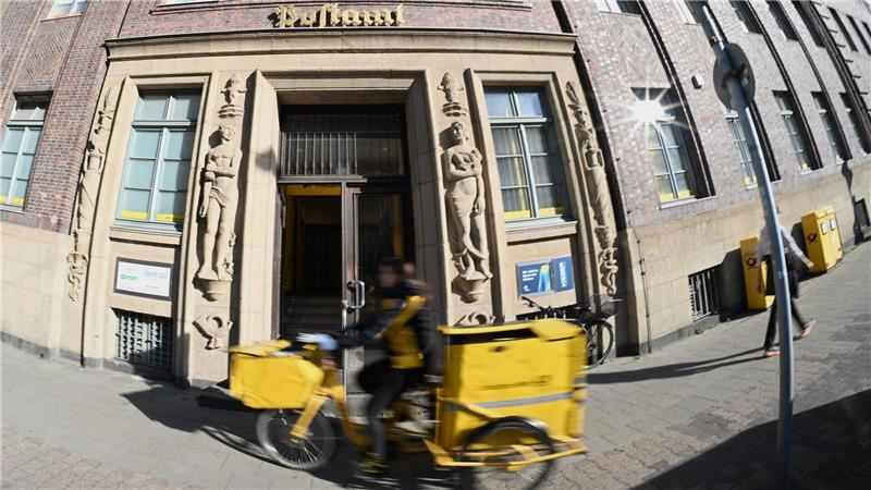 Post und Telekom haben noch Tausende Beamte Eine Briefträgerin fährt an einer Postfiliale vorbei - vielleicht ist auch sie eine Beamtin?