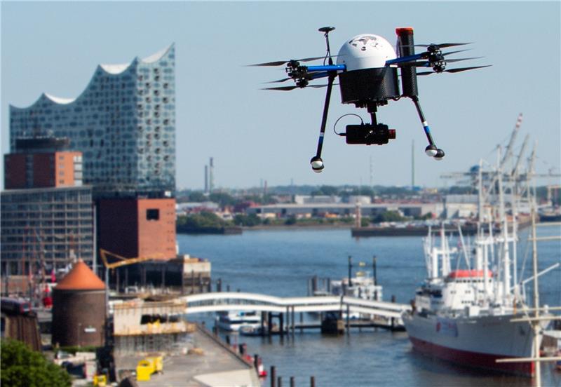 Eine Drohne mit einer montierten Kamera fliegt über dem Hamburger Hafenrand. Foto UAV Hamburg/Jan Brandes