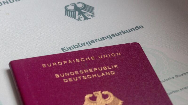 Eine Einbürgerungsurkunde von Deutschland und ein deutscher Reisepass liegen auf einem Tisch.