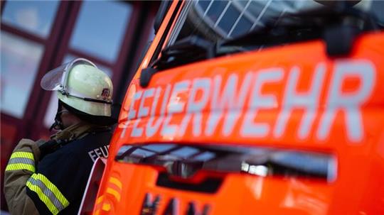 Eine Einsatzkraft der Feuerwehr steht neben einem Einsatzfahrzeug der Feuerwehr.