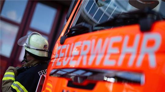 Eine Einsatzkraft der Feuerwehr steht neben einem Einsatzfahrzeug der Feuerwehr.