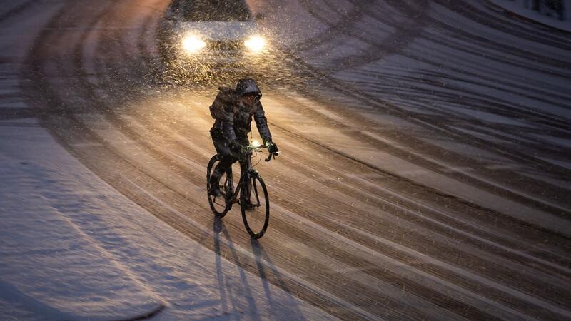 Glätte in Hamburg: Winterdienst im Einsatz Eine Fahrradfahrerin fährt am Morgen eine verschneite Straße entlang.