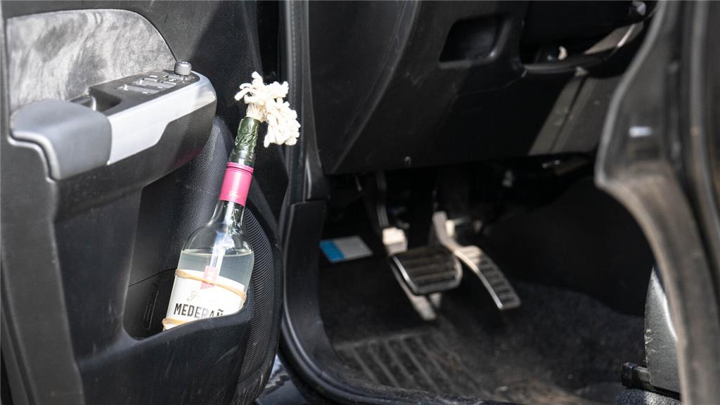 Eine Flasche mit Textilfasern im Flaschenhals steht in der Tür eines Autos. Foto...