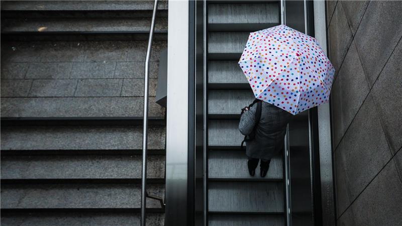 Eine Frau fährt mit ihrem Regenschirm eine Rolltreppe hinauf. Das Wetter soll in der Region Stuttgart in den nächsten Tagen wechselhaft bleiben.
