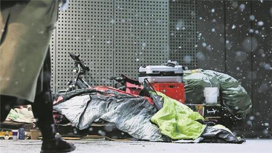 Eine Frau geht am frühen Morgen an einem Schlafplatz von obdachlosen Menschen unter dem Vordach eines Kaufhauses in der Innenstadt vorbei.
