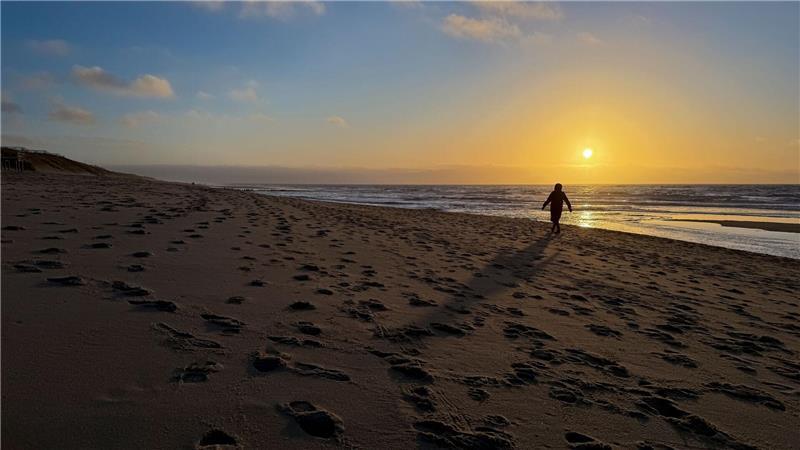 Eine Frau geht im Licht der tief stehenden Sonne am Strand bei Rantum auf Sylt spazieren.