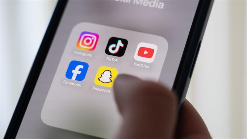 Eine Frau hält ein Smartphone, auf dessen Display verschiedene Social Media Apps angezeigt werden.