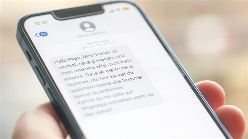 Eine Frau hält ein Smartphone in ihrer Hand, auf dessen Display eine Betrugs-SMS zu lesen ist.