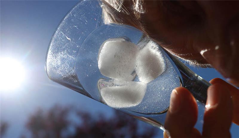 Eine Frau kühlt ihre Stirn mit einem Glas mit Eiswürfel. Foto: Karl-Josef Hildenbrand/dpa