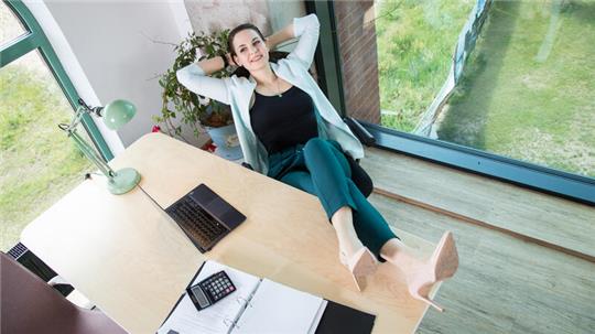 Eine Frau legt entspannt die Füße auf ihren Schreibtisch.