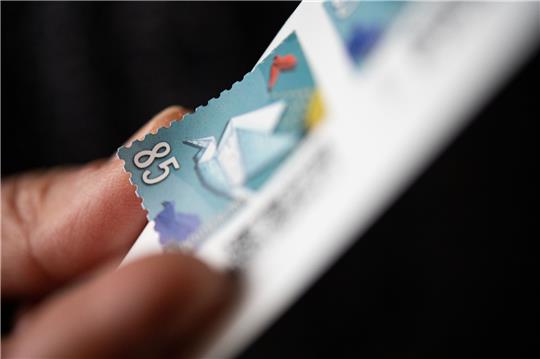 Eine Frau löst eine 85 Cent Briefmarke von einem Bogen. Das jetzige Porto gilt seit Anfang 2022, als sich der Inlandsstandardbrief von 80 auf 85 Cent verteuerte. Foto: Marijan Murat/dpa