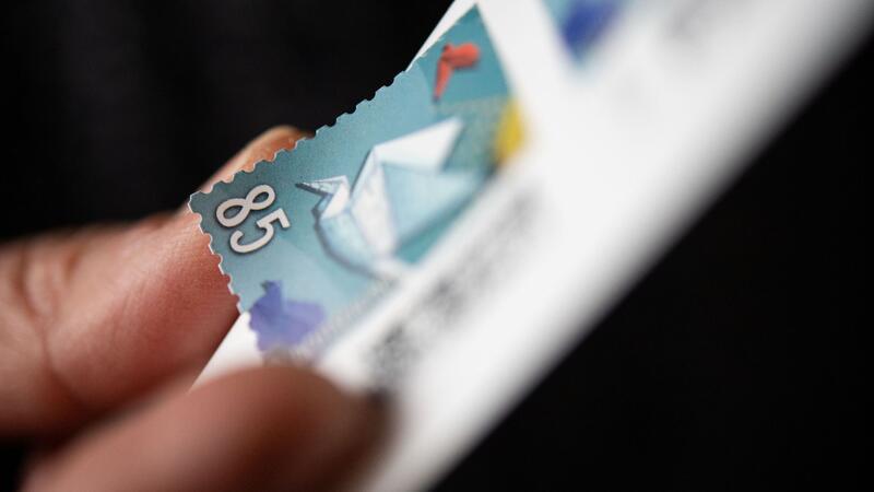 Nachfrage nach „Mobiler Briefmarke“ steigt Eine Frau löst eine Briefmarke von einem Briefmarken-Bogen, um sie auf einen Brief zu kleben.