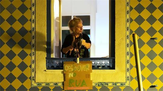 Eine Frau schlägt auf einen Topfdeckel, während sich Demonstranten versammeln, um bezahlbaren Wohnraum zu fordern.