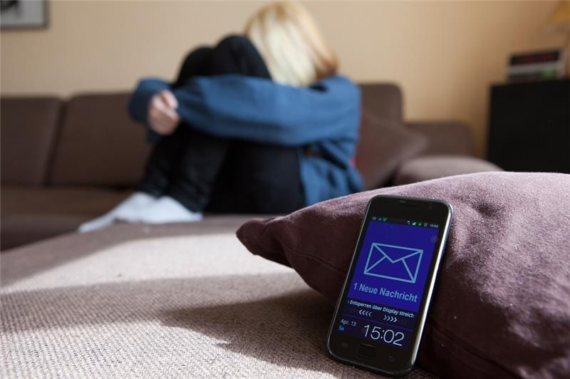 Eine Frau sitzt auf einem Sofa, während auf ihrem Smartphone eine Nachricht ankommt. Symbolfoto: Silvia Marks/dpa-tmn/dpa