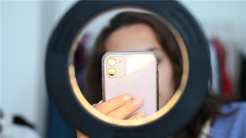 Eine Frau sitzt hinter einem Ringlicht und macht dabei Aufnahmen von sich (Symbolbild)