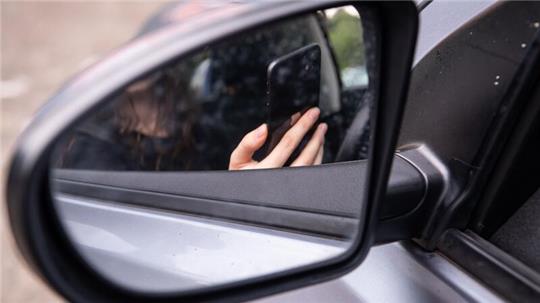 Eine Frau sitzt mit Handy am Steuer (gestellte Szene).