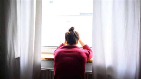 Eine Frau sitzt mit Kopf in den Händen am Fenster.