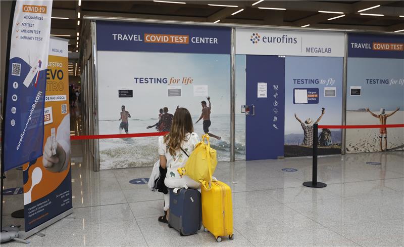 Eine Frau sitzt vor dem Testzentrum am Flughafen von Palma de Mallorca auf Koffern. Ab dem 1. August müssen alle nicht geimpften Reisenden über 12 Jahren einen negativen Test vorweisen, um nach Deutschland zurückkehren zu können. Foto: Clara Margais/dpa