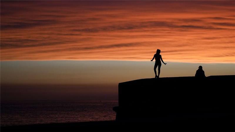 Eine Frau steht an der Uferpromenade von Montevideo in Uruguay vor dem Hintergrund des Sonnenuntergangs.