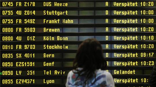 Eine Frau steht auf einem Flughafen vor einer Anzeigetafel, auf der verspätete Flüge aufgelistet werden.