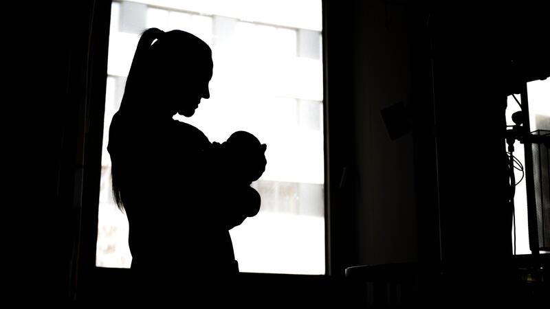 Eine Frau steht mit einem Neugeborenen am Fenster.