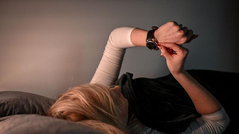 Eine Frau stellt im Bett ihre Armbanduhr um.