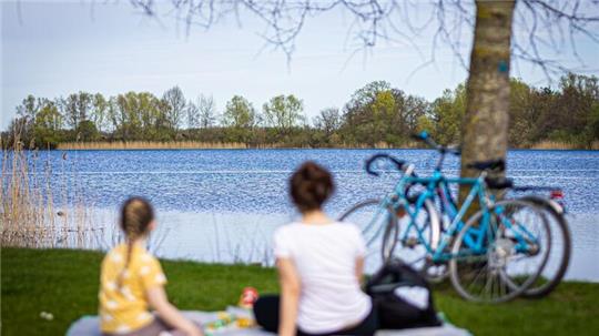 Eine Frau und ein Kind sitzen bei sonnigem Wetter am Ufer vom Hufeisensee in der Region Hannover.