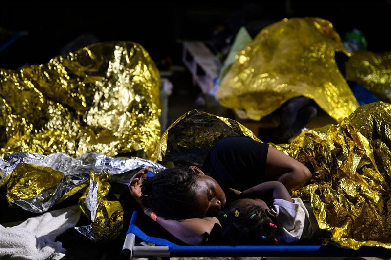 Eine Frau und ein Kind sowie weitere Menschen schlafen im Freien vor dem Erstaufnahmelager auf Lampedusa.