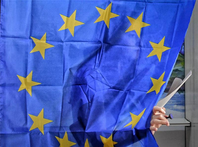 Eine Frau verlässt mit einem Stimmzettel in der Hand eine Wahlkabine mit einer Europaflagge als Vorhang in einem Wahlbüro annlässlich der Europawahl. Foto: Andreea Alexandru/AP/dpa