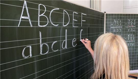 Eine Grundschülerin in Hamburg die ersten Buchstaben des Alphabets auf eine Schultafel in einem Klassenzimmer.