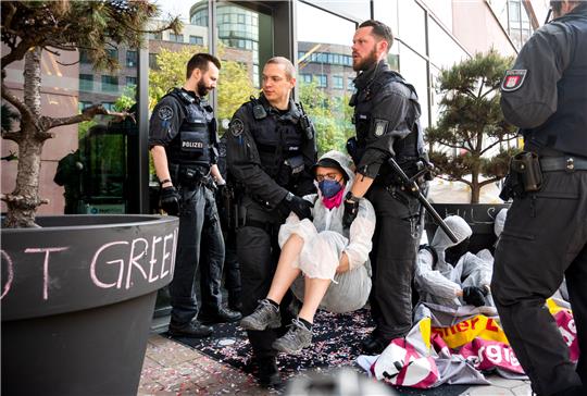 Eine Klimaaktivistin der Gruppe "Ende Gelände" wird von Polizisten weggetragen. Klimaaktivisten blockierten den Zugang zu einem Hotel, um gegen das 5th Global LNG Forum zu protestieren. Foto: Daniel Bockwoldt/dpa