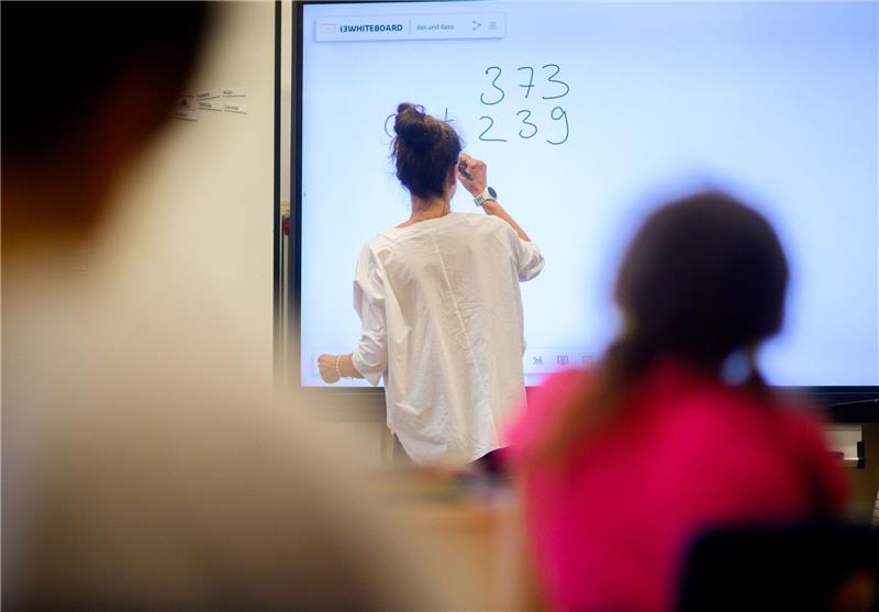 Schulleiter: Lehrkräfte vorrangig an Grundschulen einsetzen Eine Lehrerin schreibt eine Mathematikaufgabe auf eine digitale Schultafel im Klassenraum einer 4. Klasse einer Grundschule.