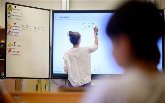 Eine Lehrerin schreibt eine Mathematikaufgabe auf eine digitale Schultafel.