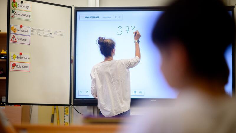 Eine Lehrerin schreibt eine Mathematikaufgabe auf eine digitale Schultafel im Klassenraum.