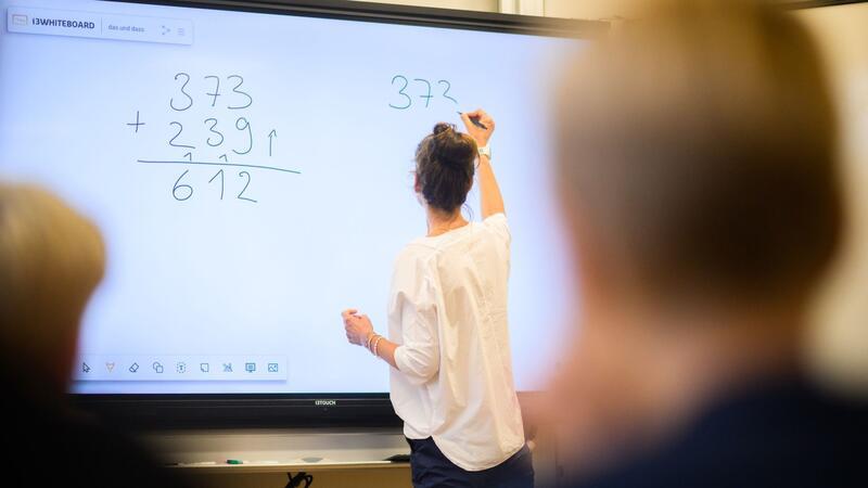 Eine Lehrerin schreibt eine Mathematikaufgabe auf eine digitale Schultafel.