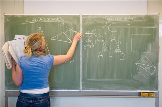 Eine Lehrerin schreibt mit Kreide an die Tafel.