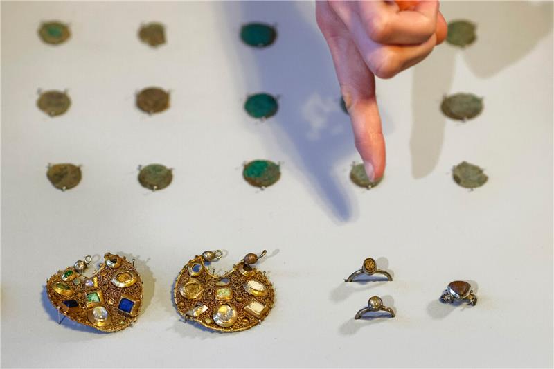 Vor 800 Jahren versteckt: Münzen und Schmuck bei Haithabu entdeckt Eine Mitarbeiterin des Archäologischen Landesamtes Schleswig-Holstein deutet mit dem Finger auf zwei Ohranhänger. Mitarbeiter des Landesamtes hatten mit Hilfe von Detektoren den Schmuck aus der Zeit um 1100 gefunden. Laut Landesamt wurde der Schmuck vermutlich vor rund 800 Jahren von einem Reisenden versteckt. Foto: Frank Molter/dpa